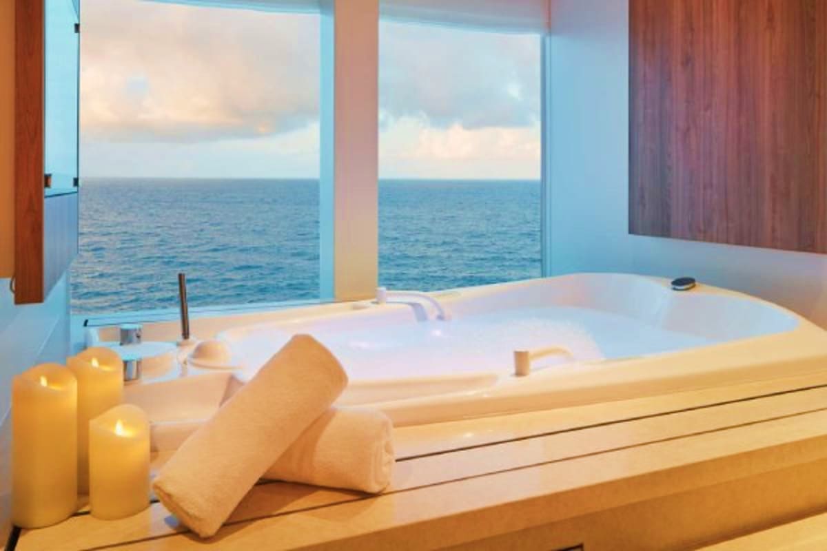 Luxury cruise ship bathroom with ocean view, white bathtub, lit candles, and rolled towels overlooking Mediterranean Sea